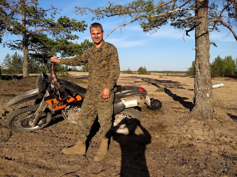 Marine in combat utilities standing next to motorcycle in Finnish terrain